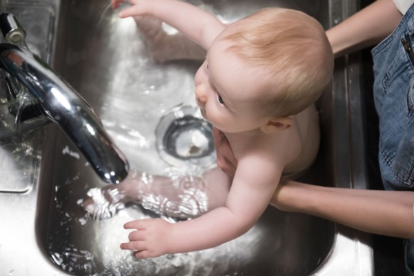Mother bathing Caucasian baby son in sink