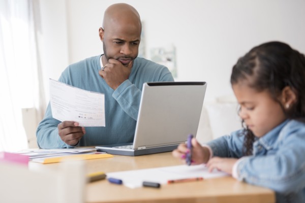 Daughter coloring with crayons while father uses laptop