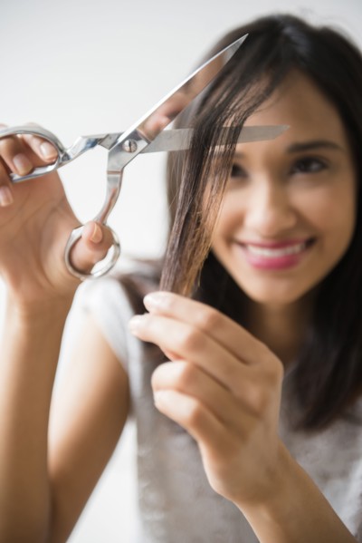 Mixed Race woman cutting hair with scissors