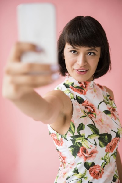 Hispanic woman wearing floral dress posing for cell phone selfie