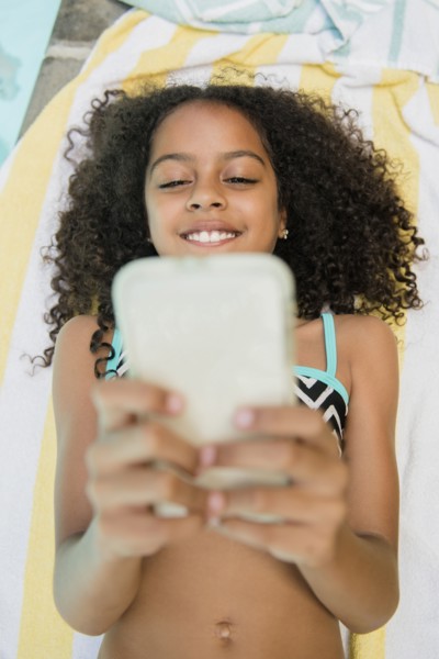 Smiling Hispanic girl texting on cell phone at swimming pool