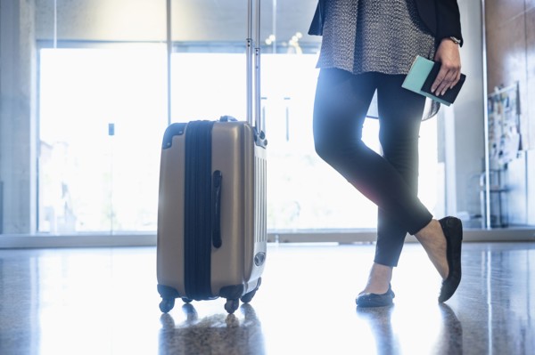 Hispanic woman holding passport standing with suitcase in airport