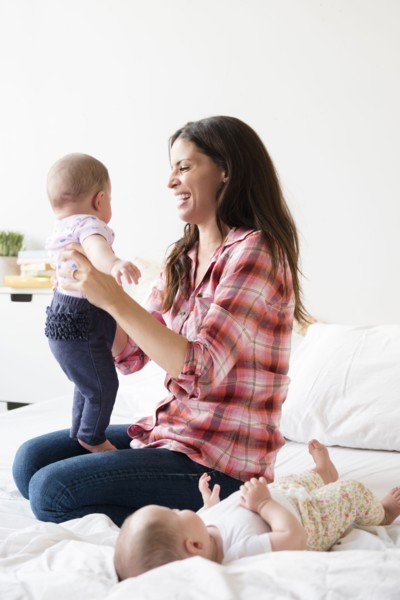 Caucasian mother playing on bed with twin baby daughters