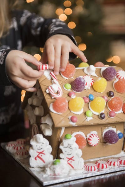 Hands of Caucasian girl decorating gingerbread house with candy