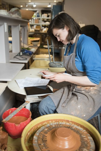 Caucasian woman reading paperwork near pottery wheel