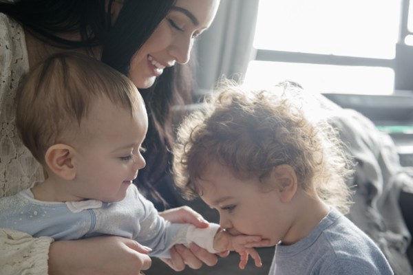 Caucasian mother watching son kiss hand of baby brother
