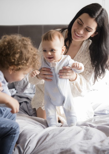 Caucasian mother kneeling on bed playing with sons