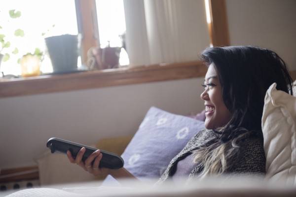 Smiling Mixed Race woman holding remote control and watching television