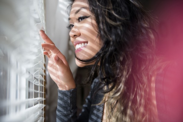Mixed Race woman peeking out window behind blinds
