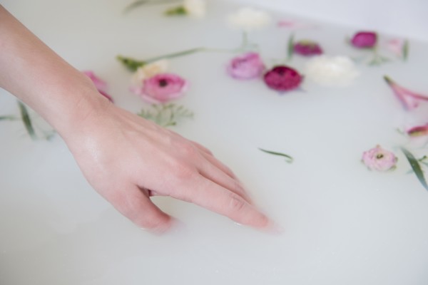 Hand of Caucasian woman in milk bath with flowers