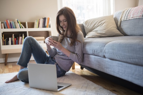 Caucasian woman sitting on floor with coffee and laptop