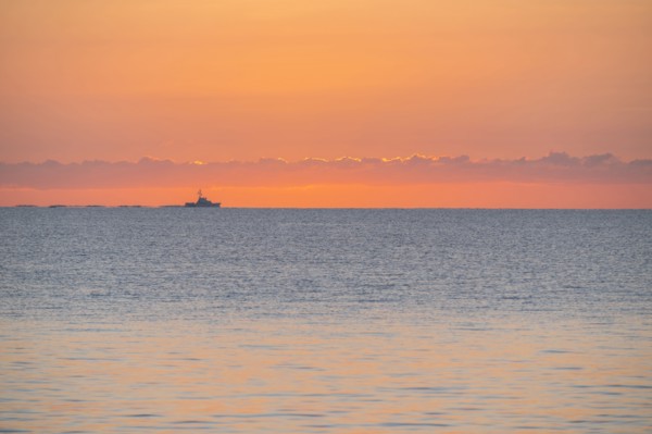 Calm sea at sunrise with fishing boat in distance