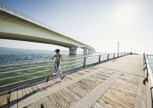Rear view of woman jogging on bridge on sunny day