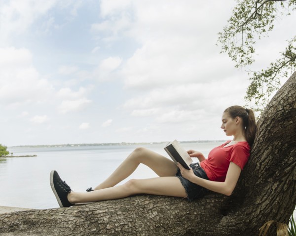 Woman sitting on tree and reading book