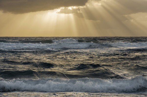 Sun rays streaking from clouds over ocean waves