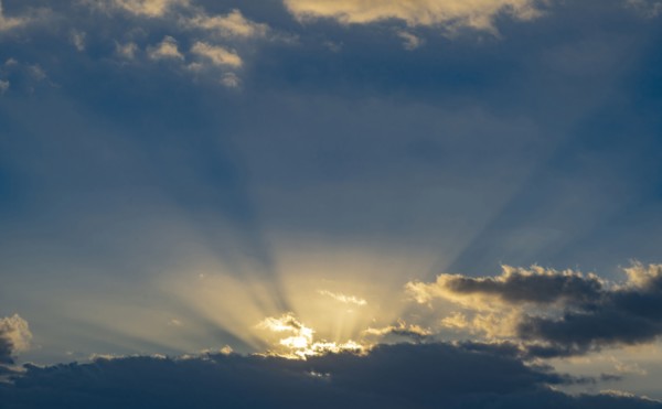 Sun rays streaking upwards from clouds against sky
