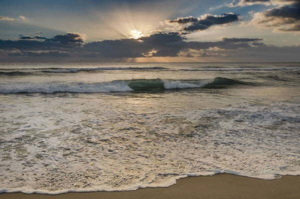 Rising sun shining through clouds above ocean