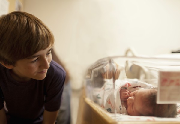 Boy (12-13) looking at newborn baby sister (0-1 months) in incubator