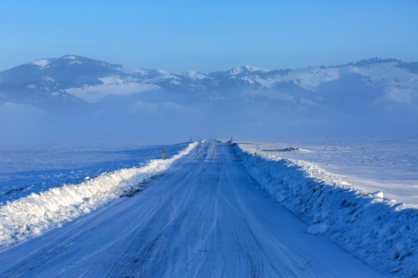 Snow covered rural road leading to mountains