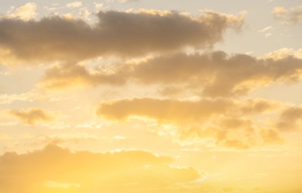 Cumulus clouds against pale golden sky at sunrise