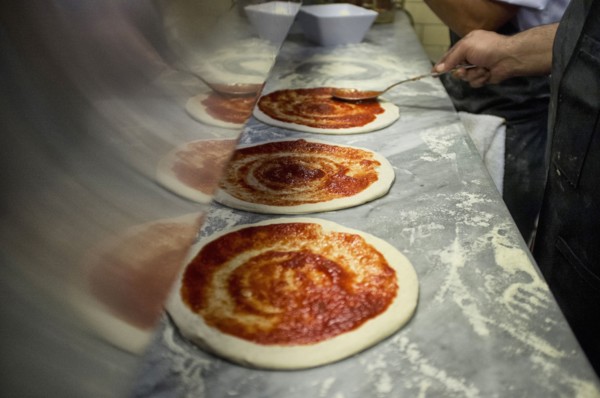 Man putting tomato sauce onto fresh hand made pizzas