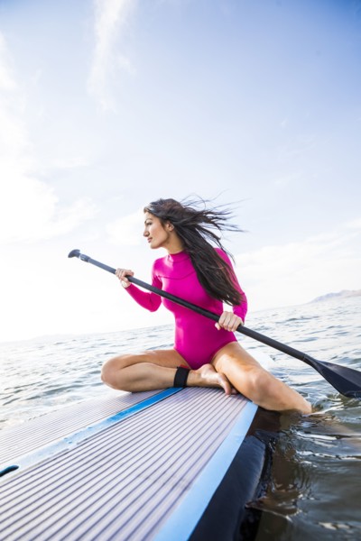 Woman in pink swimsuit sitting on paddleboard on lake