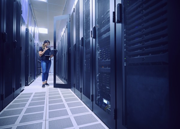 Female technician using laptop and phone in server room
