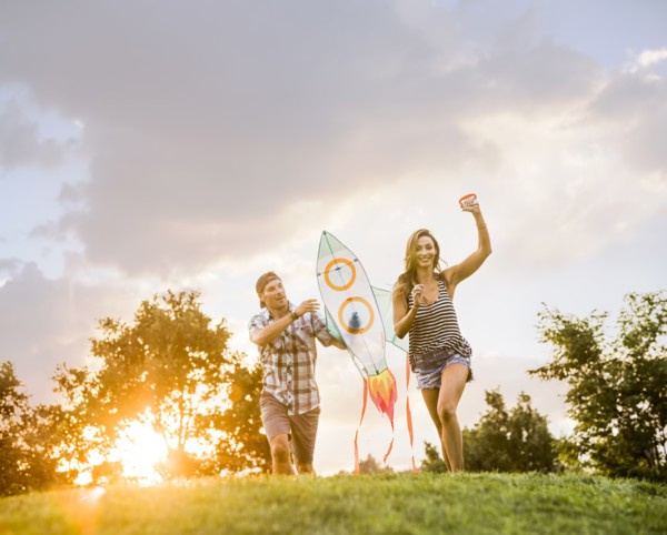Woman and man running with kite in park at sunset