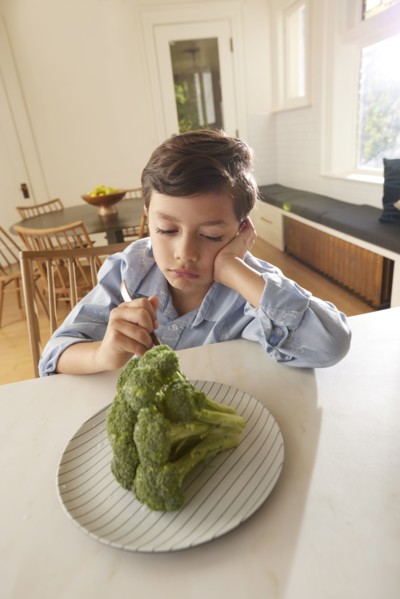 Displeased boy looking at broccoli on plate