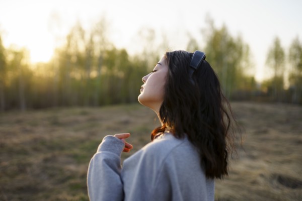Side view of woman listening to music in meadow at sunset