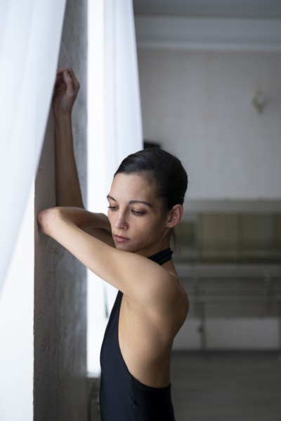 Ballerina leaning on wall with arms raised
