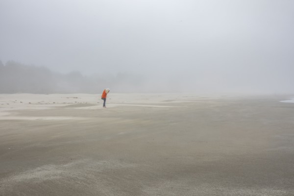 Woman in orange jacket standing on foggy beach