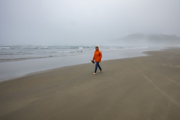 Woman in orange jacket walks along foggy beach