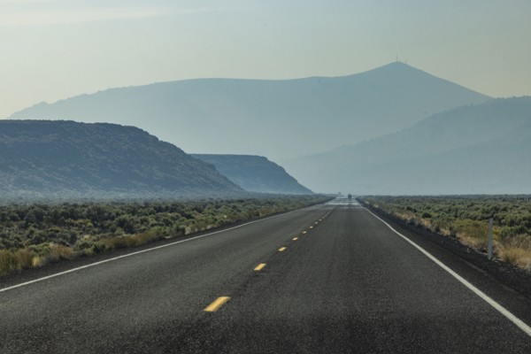 Empty highway leading through desert with mountains in background