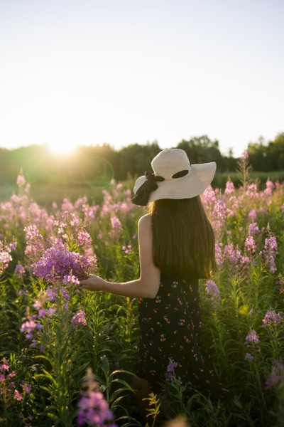 Rear view of woman in straw hat standing in meadow at sunset