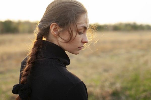 Side view of serious woman standing in field at sunset
