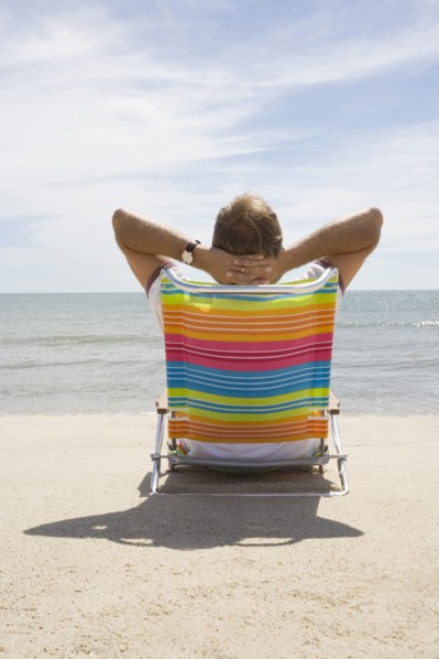 Rear view of man relaxing on deck chair on sandy beach, Nantucket, Massachusetts, USA