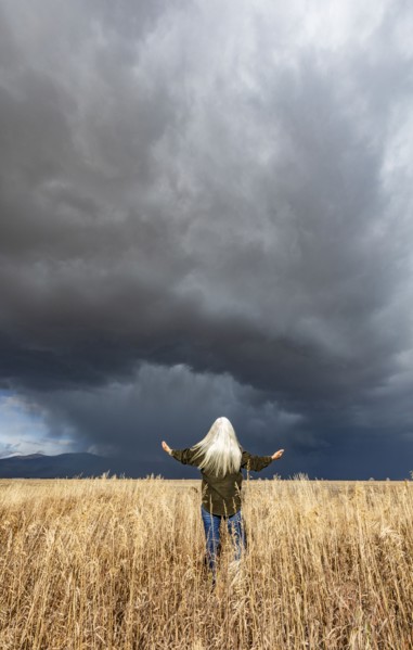 Rear view of woman standing in fall grasses under stormy sky, Fairfield, Idaho, USA