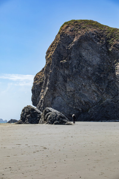 USA, Oregon, Brookings, Rear view of woman walking by huge rocks on Oregon beach