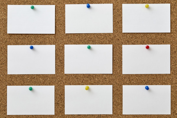 Blank pieces of paper attached to cork board with colorful push pins