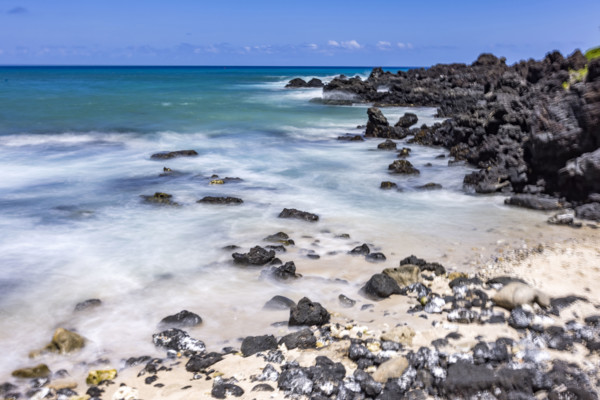 Motion blurred ocean waves washing rocks on beach. Kona, Hawaii, USA.