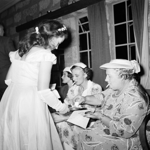Anyone for cake?. A bridesmaid offers cake to a group of smoking female guests at the