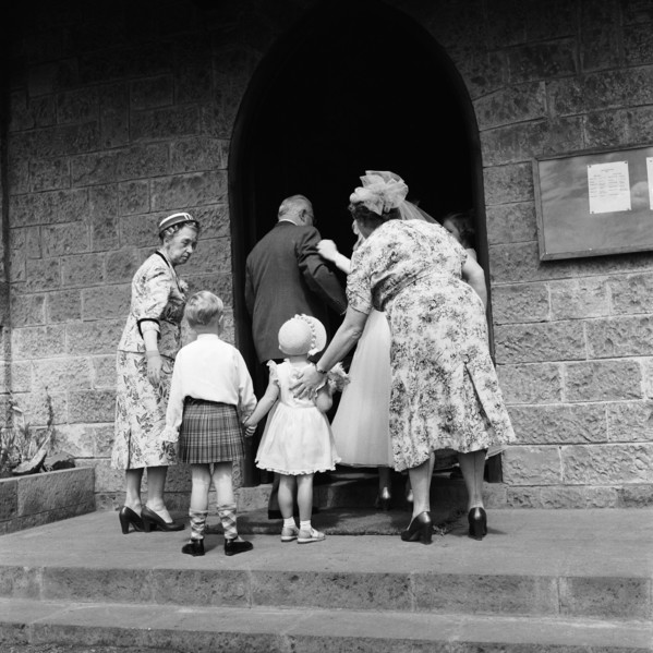 Ushered in. Two smartly dressed women usher a young boy and girl into a church on the occasion of