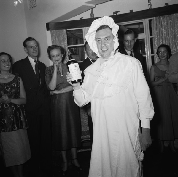 Baby costume. A man wears a fancy dress baby costume at the Archer's New Year party. He holds a