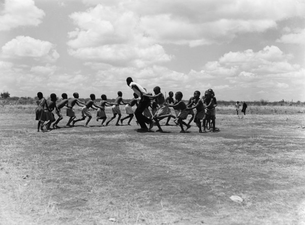 A train of children. A train of children wearing shorts hold onto one another as they run around in
