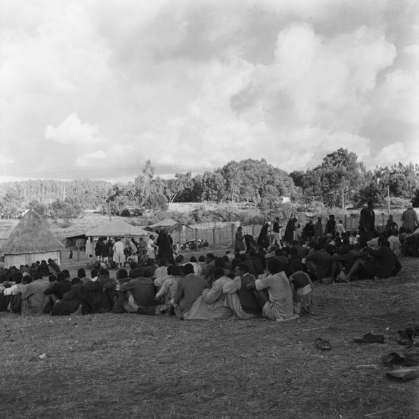 Prisoners in camp. Prisoners sit together in tightly packed lines in a fenced camp watched over by