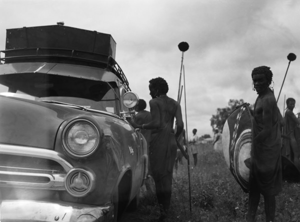 Maasai and Ford. Maasai warriors holding spears and shields congregate on the roadside near a Ford