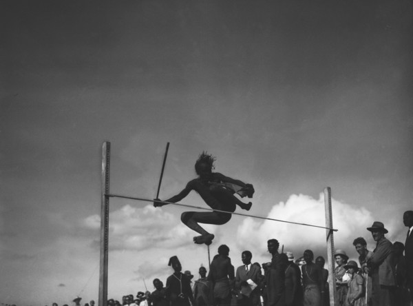 High jump. A man holding a baton attempts the high jump at a 'ngoma', a word meaning drum that is