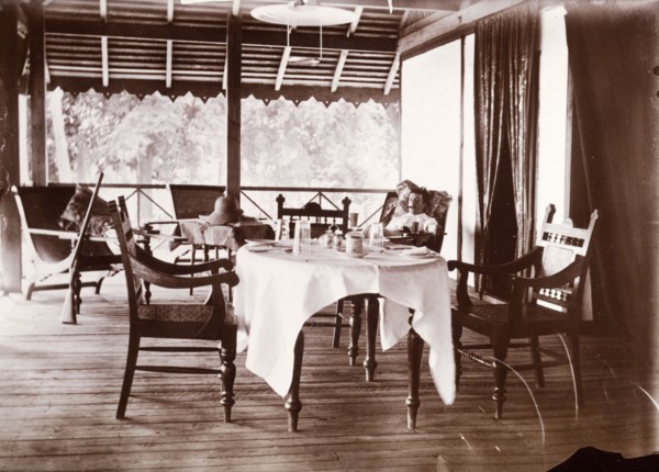 Colonial veranda. A European man smokes a cigar as he reclines in a chair on a colonial veranda.