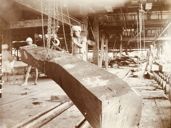 Manoevering teak logs at a timber yard. Two labourers manoeuvre a processed timber beam using a